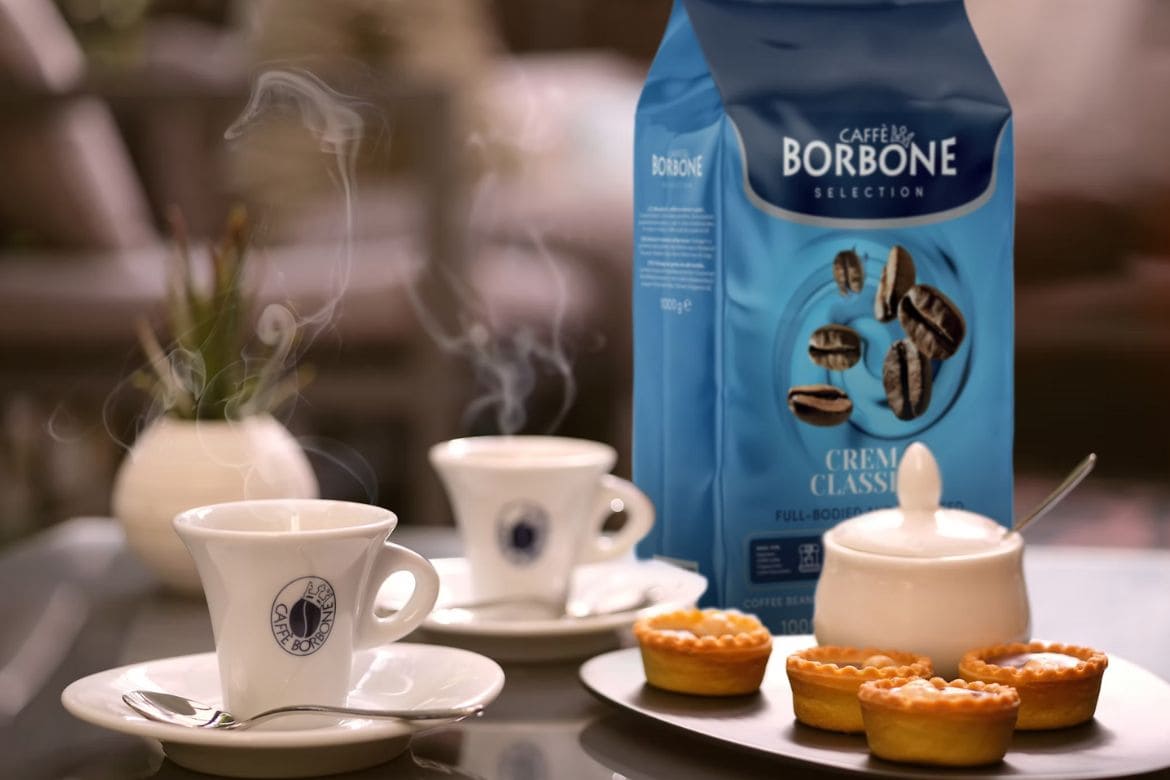 Borbone Caffè kava u keramičkim šalicama s pakiranjem kave i kolačićima na stolu
