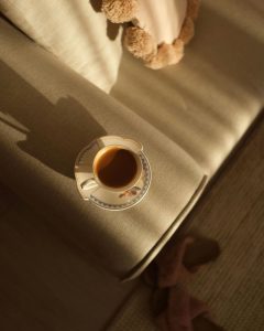 Šalica svježe pripremljenog espressa na naslonu kauča obasjana jutarnjim suncem - inspiracija za kavu kod kuće.