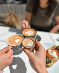 Tri osobe uživaju u kavi s latte artom na sunčanoj terasi uz doručak