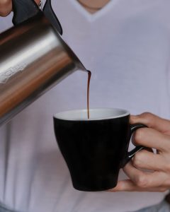Kava se ulijeva iz moka kafetijere u crnu keramičku šalicu