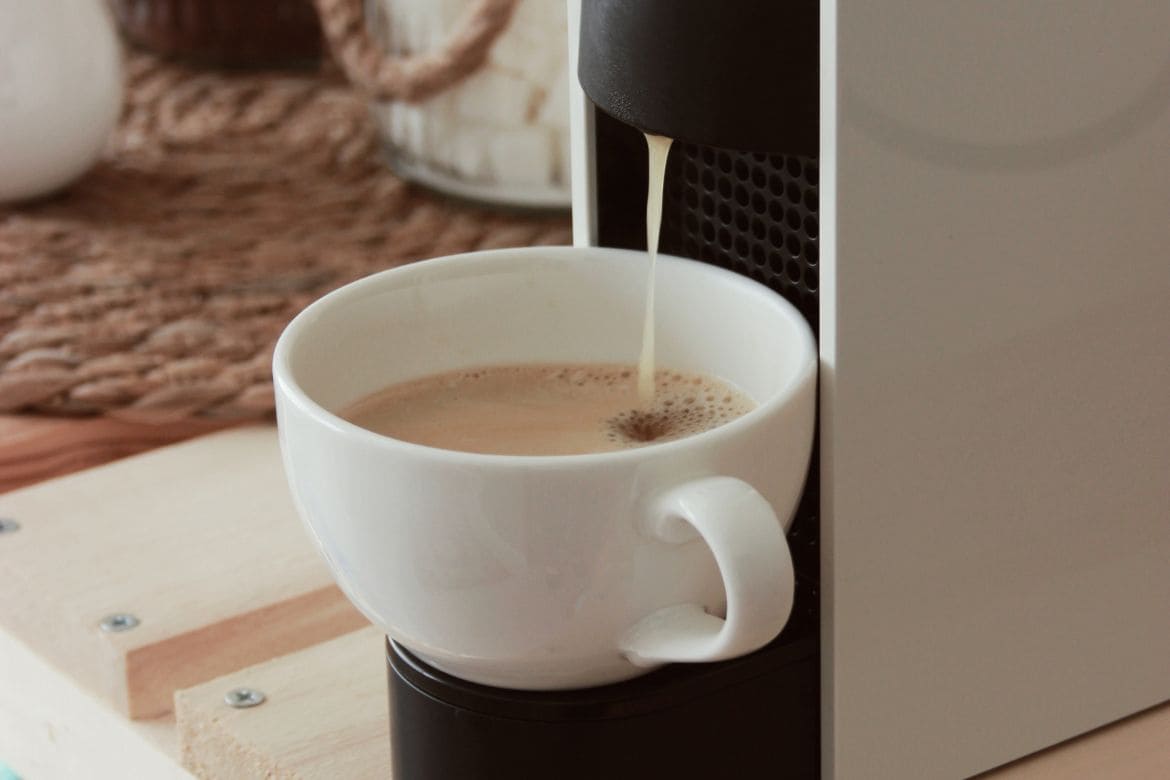 Bijela šalica ispod kapsula aparata dok se priprema espresso kava
