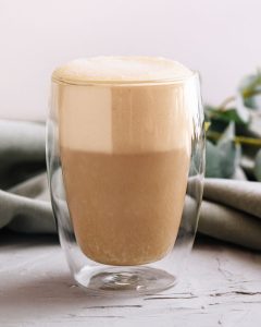 Staklena šalica s kremastom kavom i bogatom pjenom na svijetloj podlozi